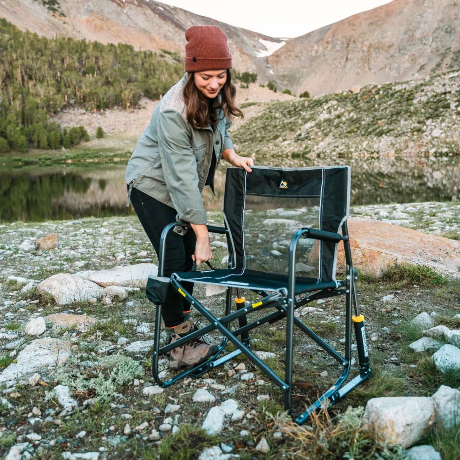 A woman in a beanie unfolding a black Freestyle Rocker near a body of water.