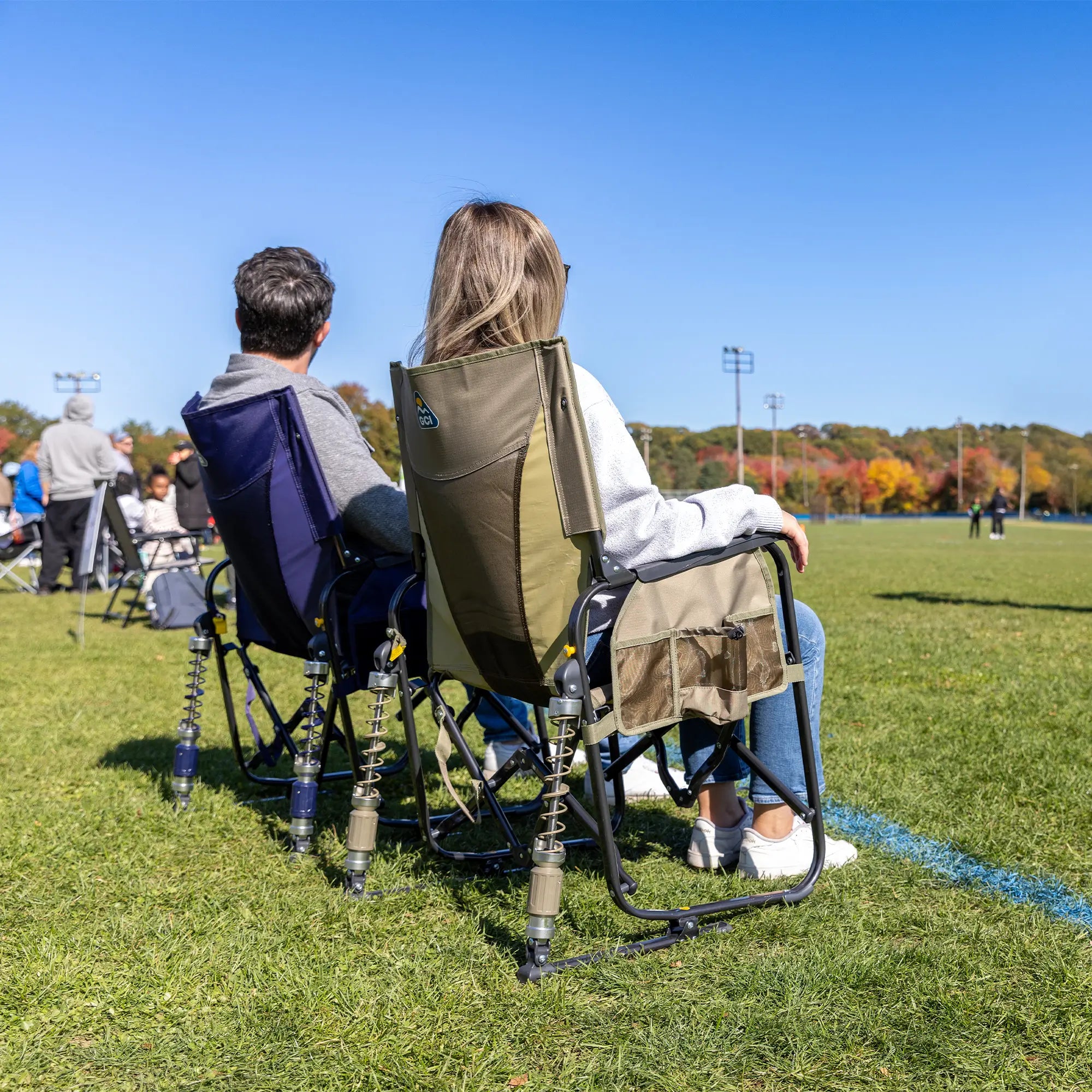Two people sitting in adjustable rocker chairs while watching a soccer game.
