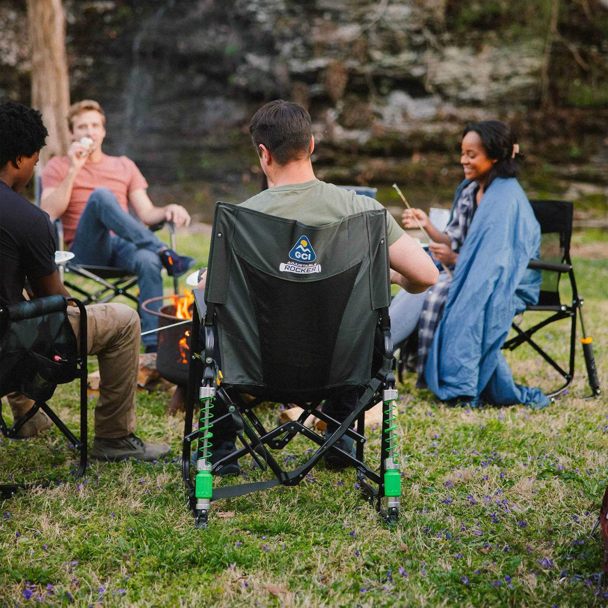 A group of people gathered around a campfire while sitting in adjustable rockers.