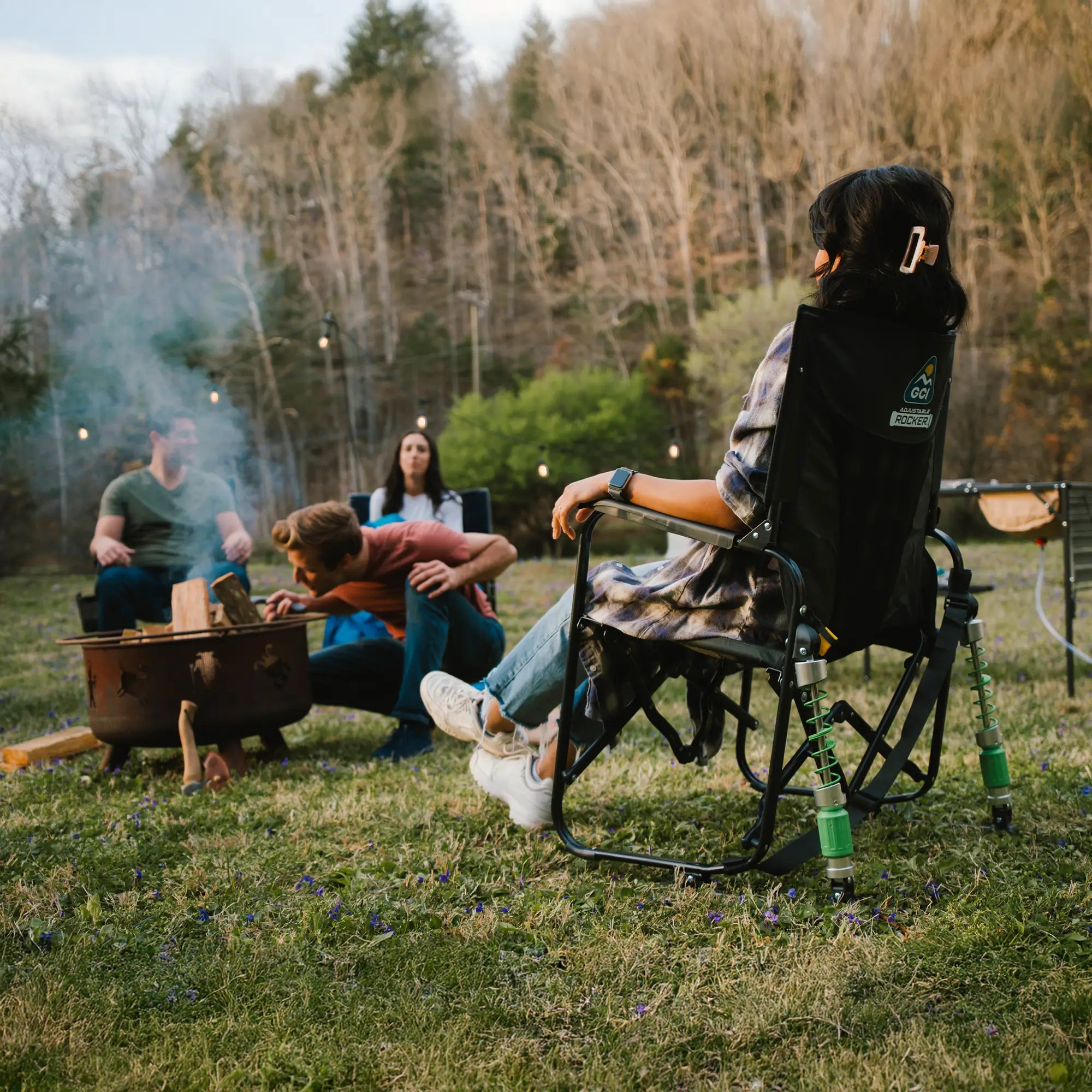 A group of people gathered around a campfire while sitting in adjustable rockers.