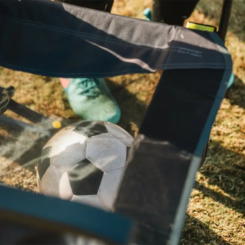 A soccer ball rests on the mesh seat of an Adjustable Rocker, with cleats visible behind