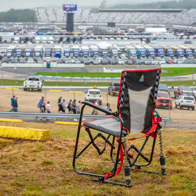Adjustable Rocker chair sits empty on a grassy hill with a racetrack and crowd in the background.
