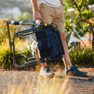 Man walks on a path carrying a folded navy Adjustable Rocker chair by its handle.