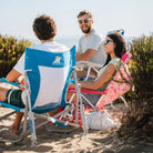 Man relaxing in a Saybrook Blue Beach Rocker, chatting with friends on a sunny beach.
