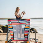 Striped Beach Rocker Chair sitting empty on the sand, with a person playing with a football in the background.
