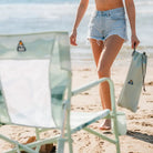 Close-up of a green Beach Rocker Chair with a person holding a Sunshade Accessory bag.