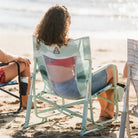 Woman sitting on a green Beach Rocker Chair at the beach, facing the water.