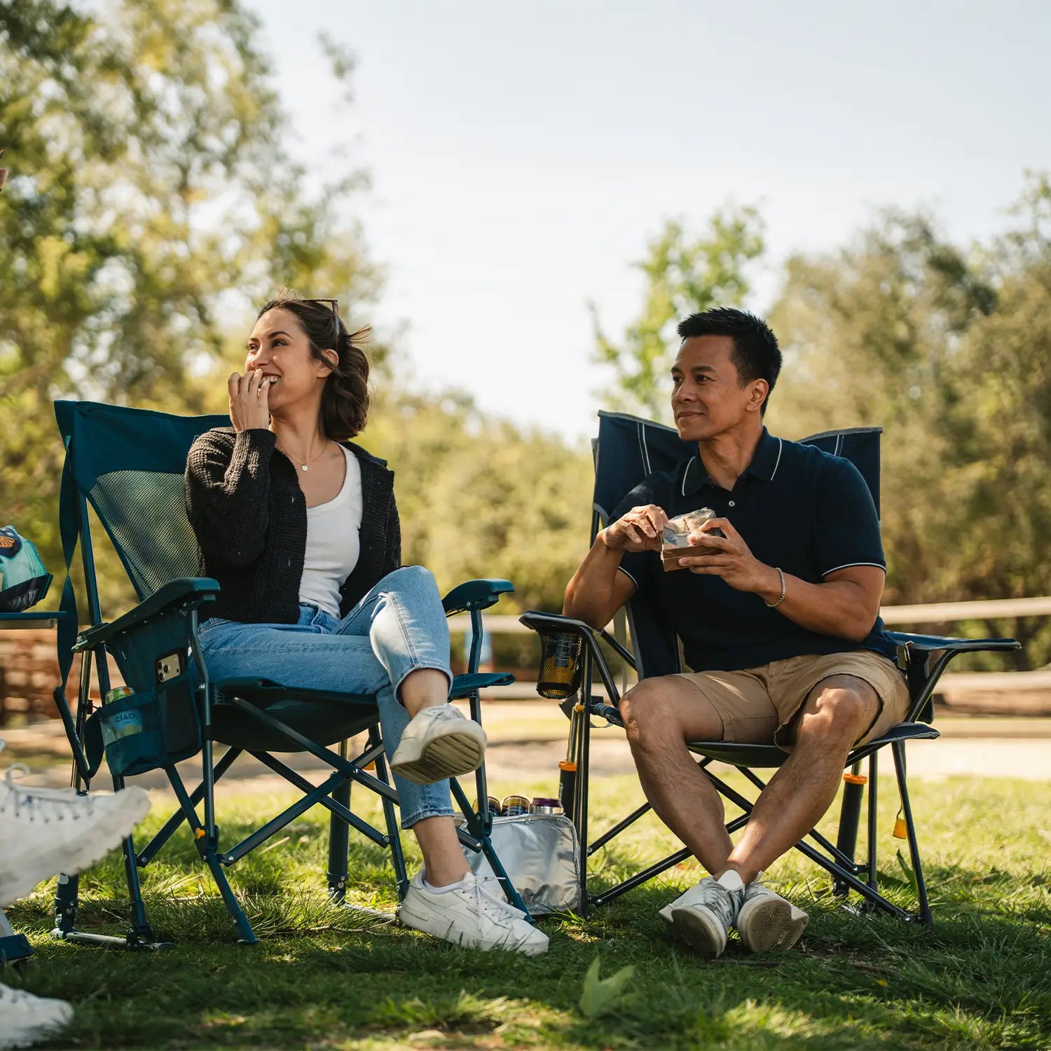 A couple enjoying snacks at a park while they sit in their Comfort Pro Rocker and BreezeRocker.