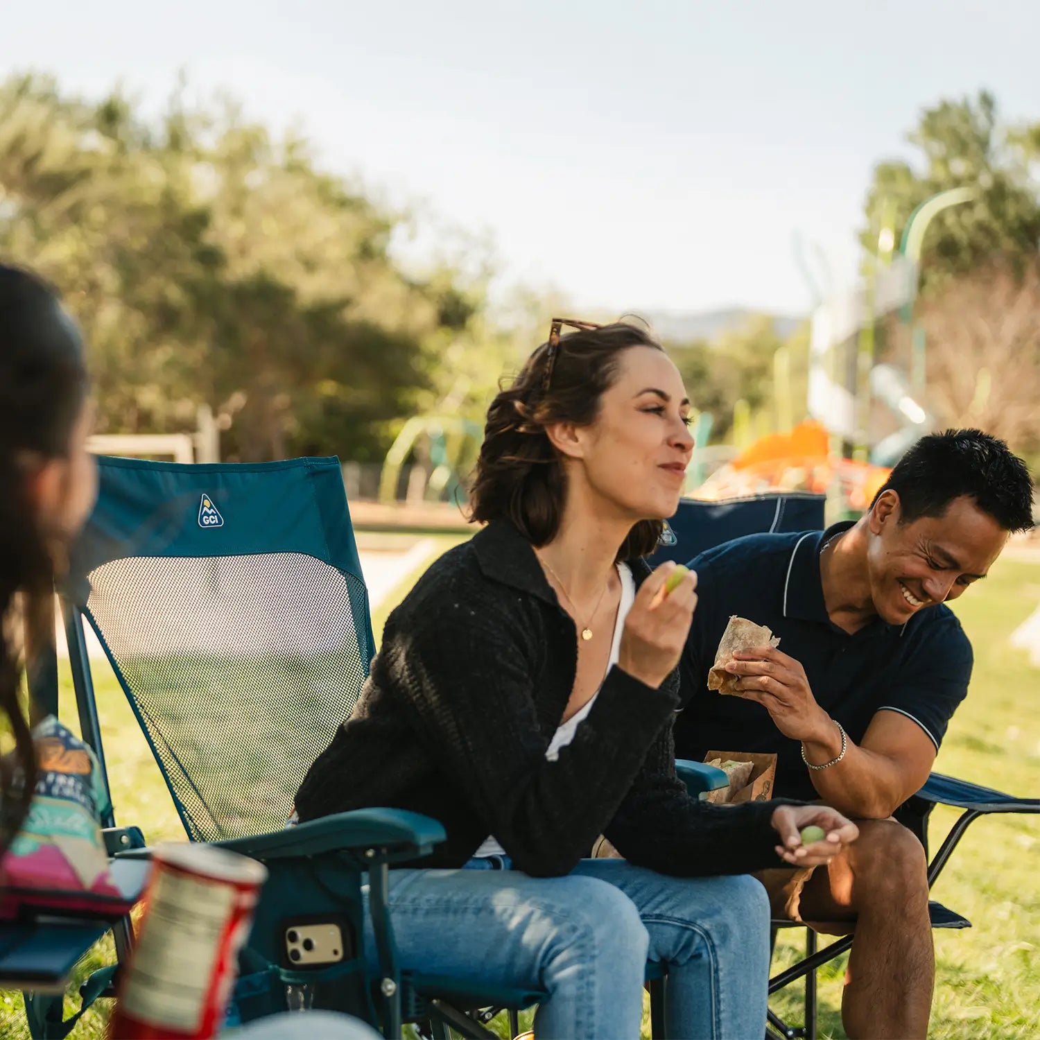 A group sitting together near a playground as they enjoy snacks that are on the Compact Camp Table 20.