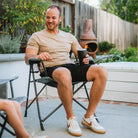 Man relaxing outdoors in a Comfort Pro Chair with a drink in hand, smiling in a backyard setting.