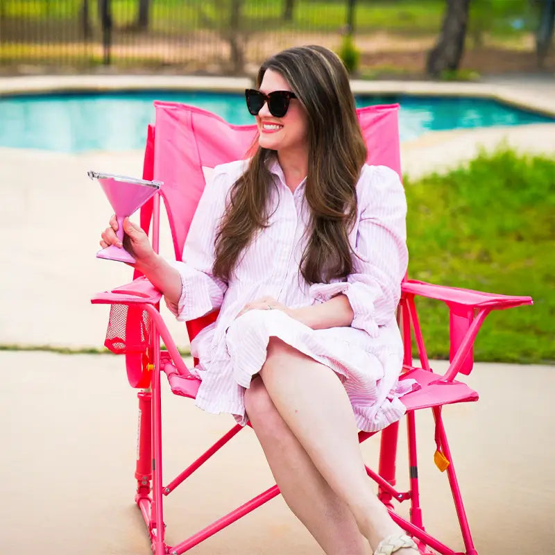 Woman relaxing by the pool with a pink drink in a blush GCI Comfort Pro Rocker chair, smiling in sunglasses.