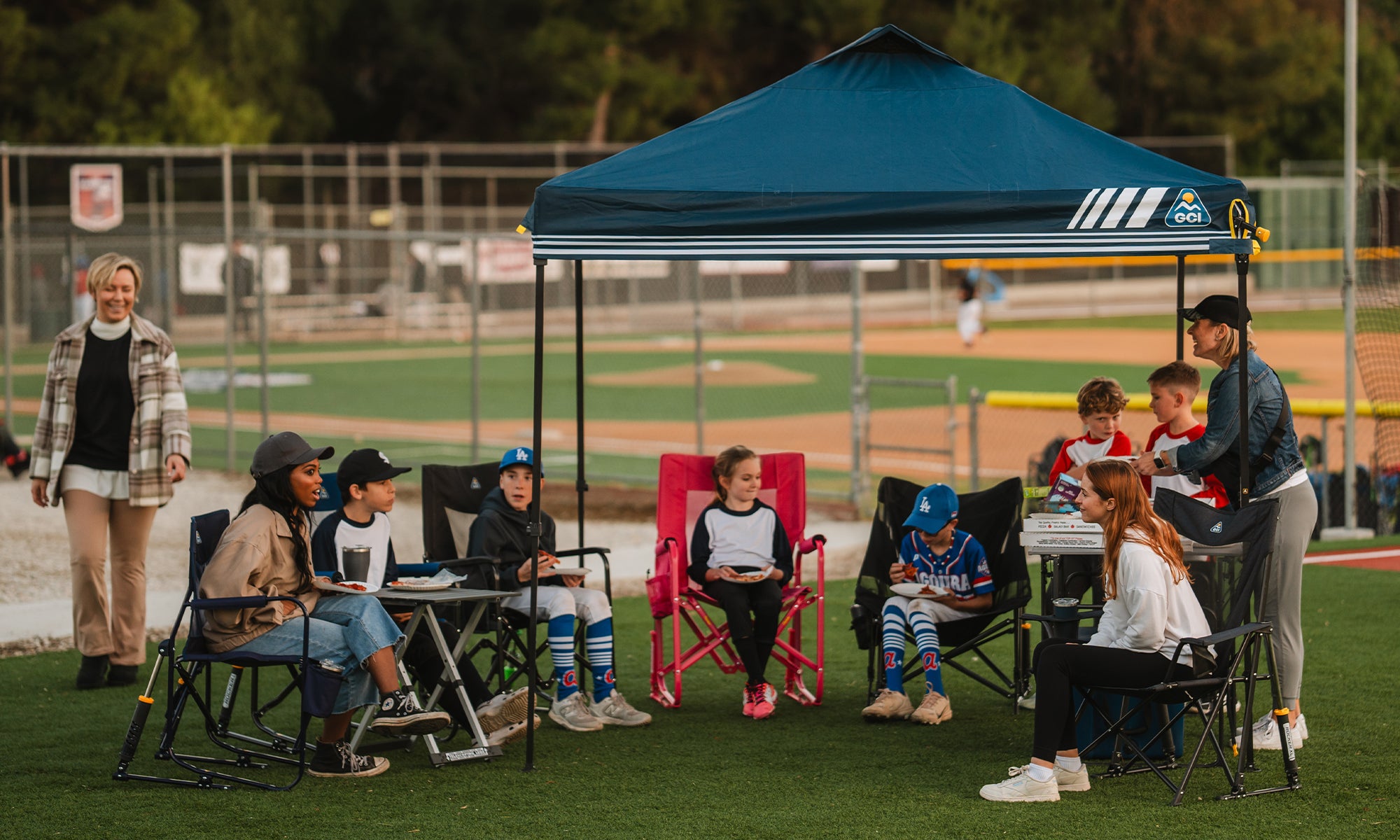 A group of baseball players and their family sitting under the levrup canopy with their GCI Outdoor chairs.