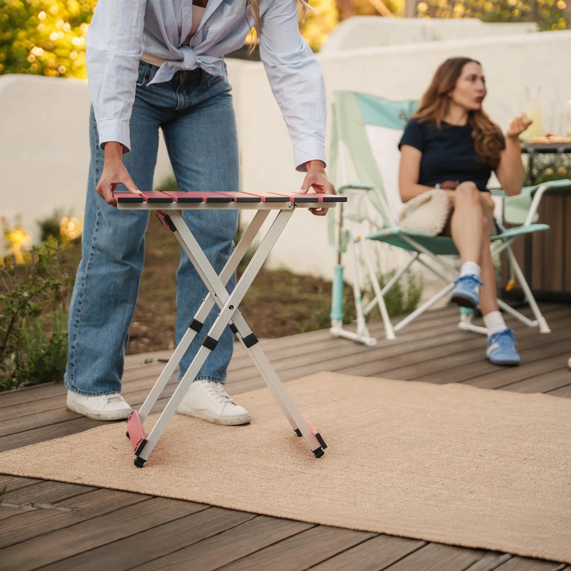 A woman setting up a coral compact camp table 20 in a backyard setting.