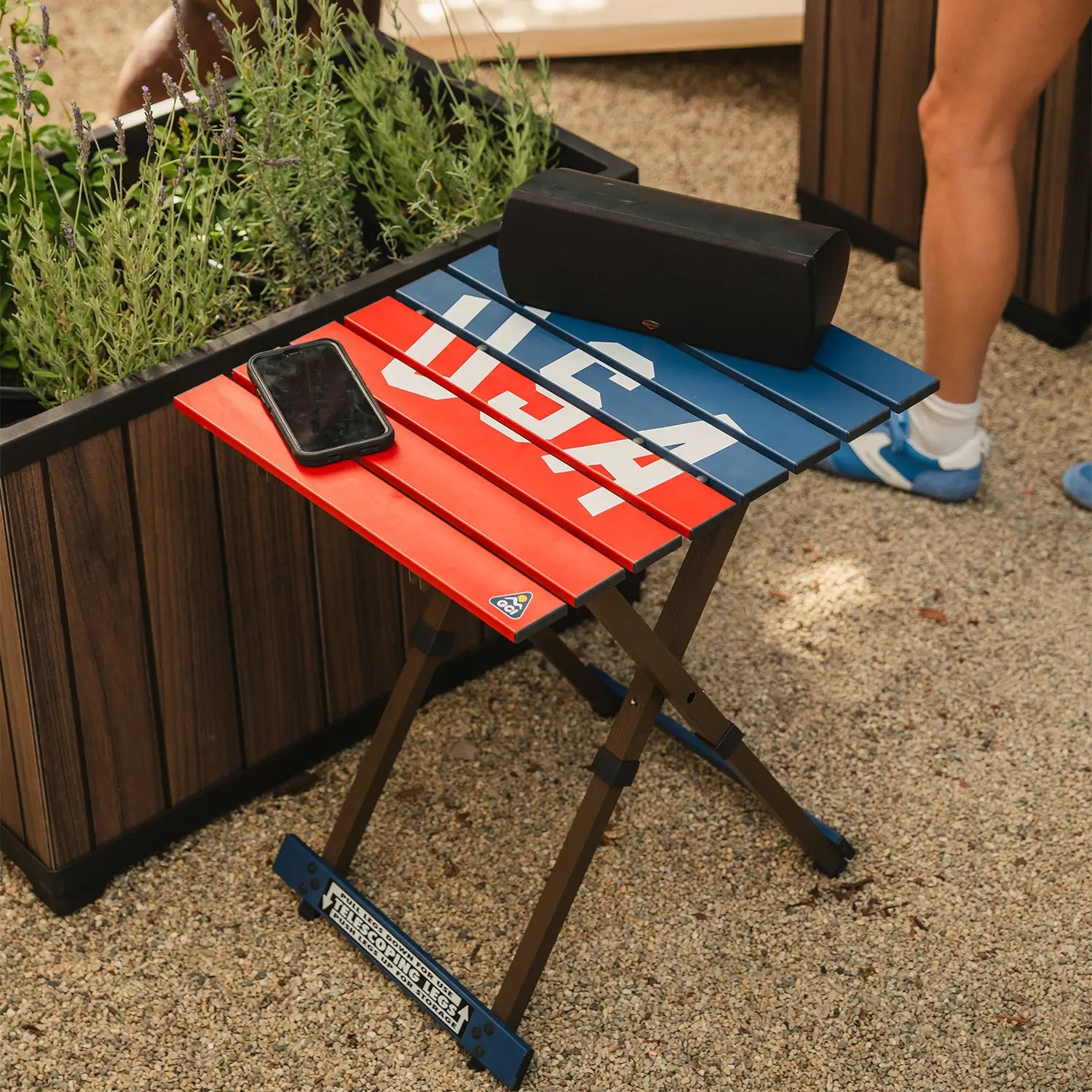 A speaker and phone resting on a USA Deluxe Compact Camp Table.