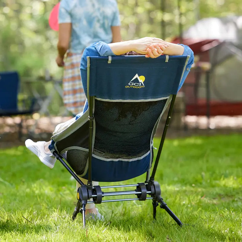 A person sitting in a compack rocker with their hands raised above their head as they watch a group play games in front of them.