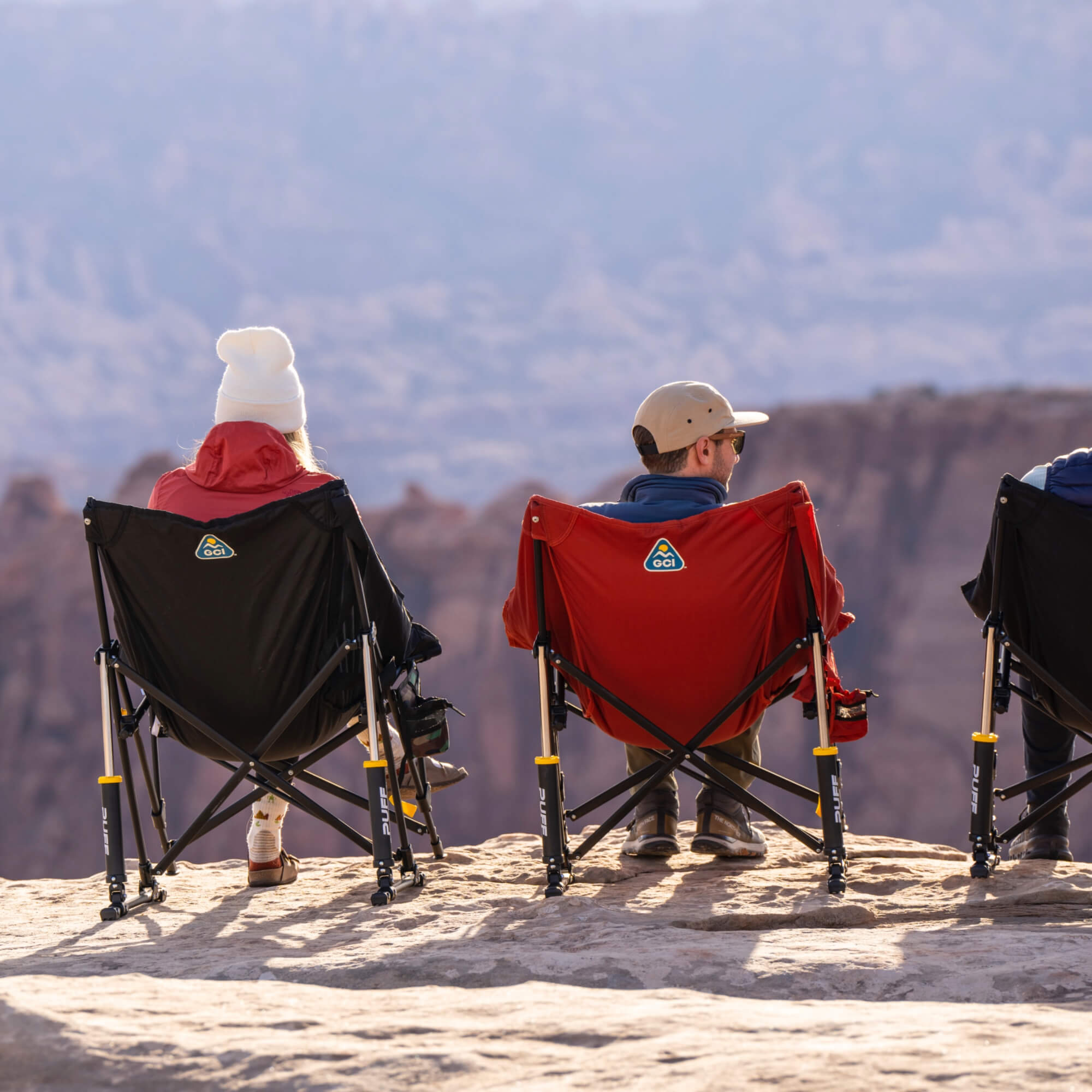 A group of people sitting in multi colored puff rocker chairs near a cliff.