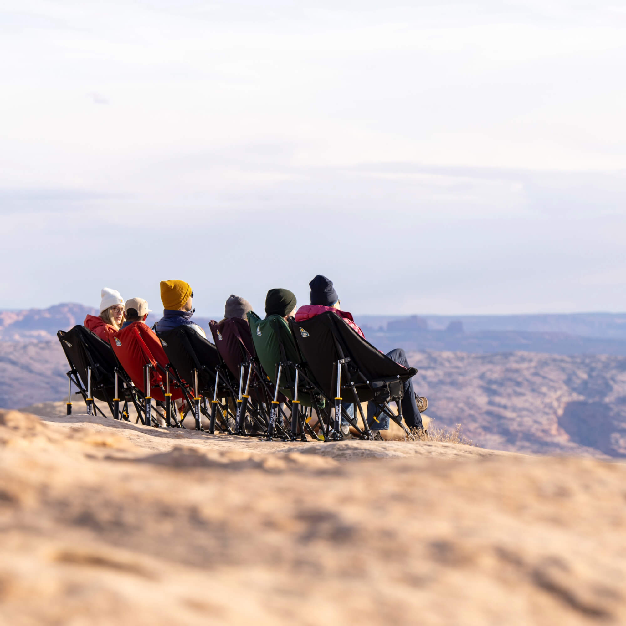 A group of people sitting in multi colored puff rocker chairs near a cliff.