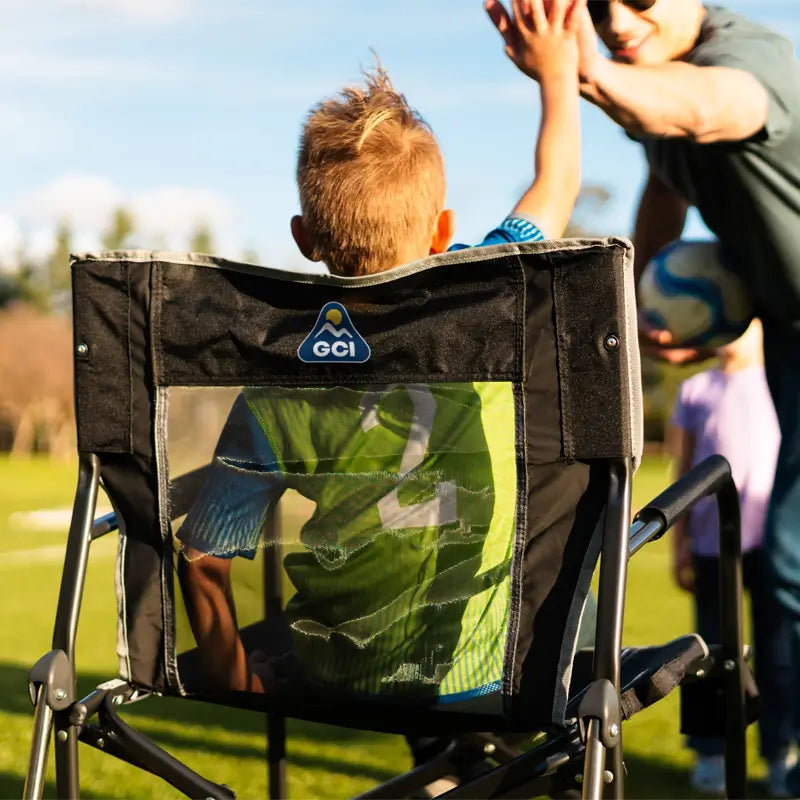 Child in a black Freestyle Rocker gives a high five on a sunny soccer field, wearing a green jersey with number 4.