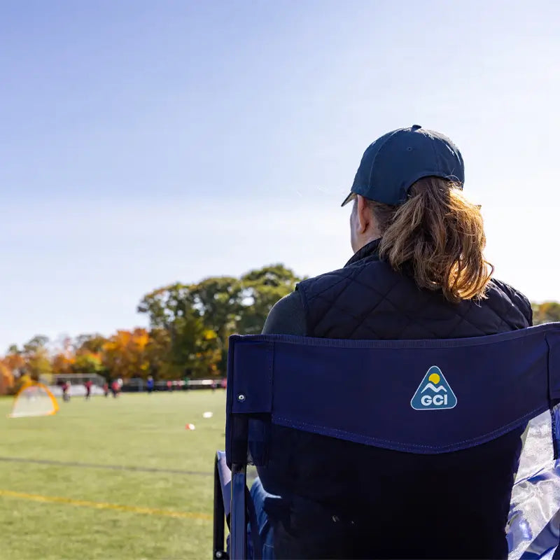 Woman watches a soccer game from a Rich Blue Freestyle Rocker Elite chair on a sunny day.