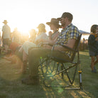 Group of people enjoying an outdoor concert seated in indigo Freestyle Rocker XL chairs at sunset.