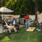 Two people sitting in a black freestyle rocker xl while watching two others play corn hole in front of them.