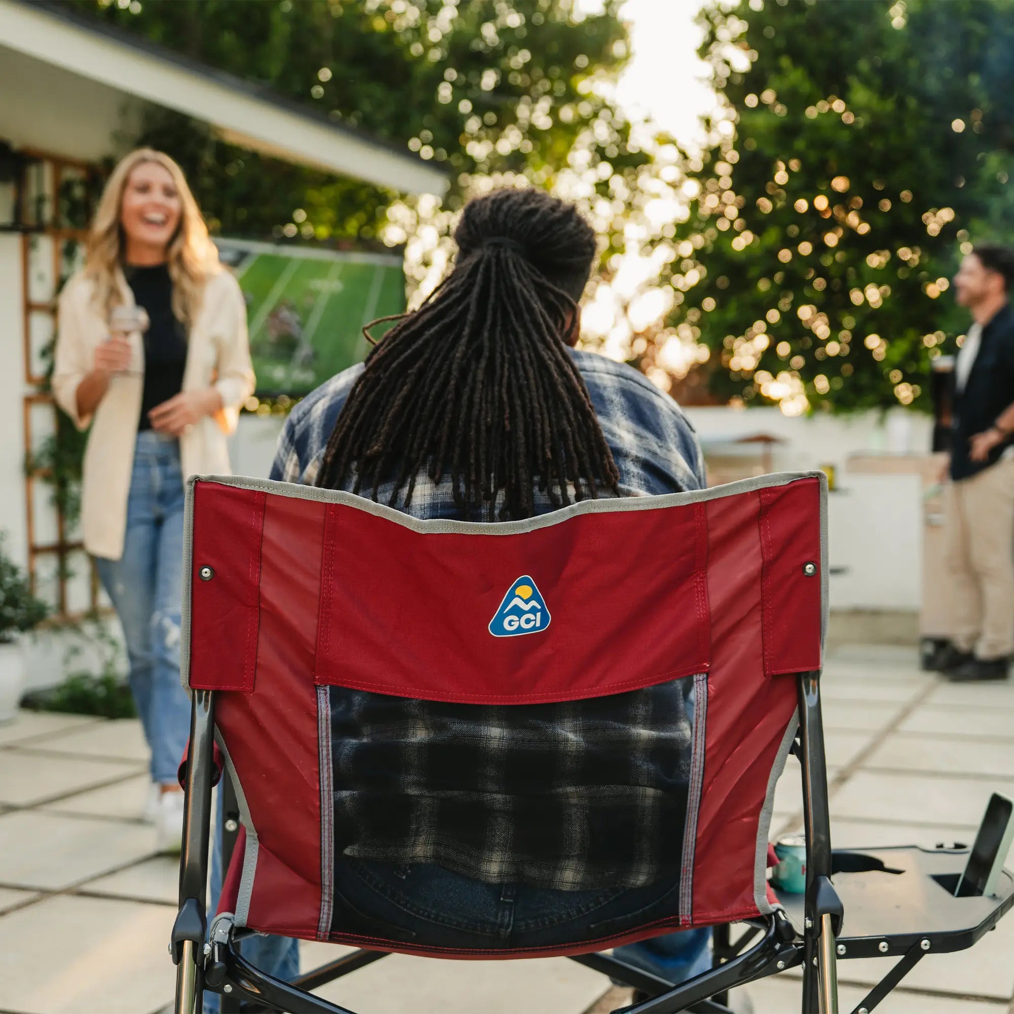 The back of a man watching a football game while sitting in a red freestyle rocker xl with side table.
