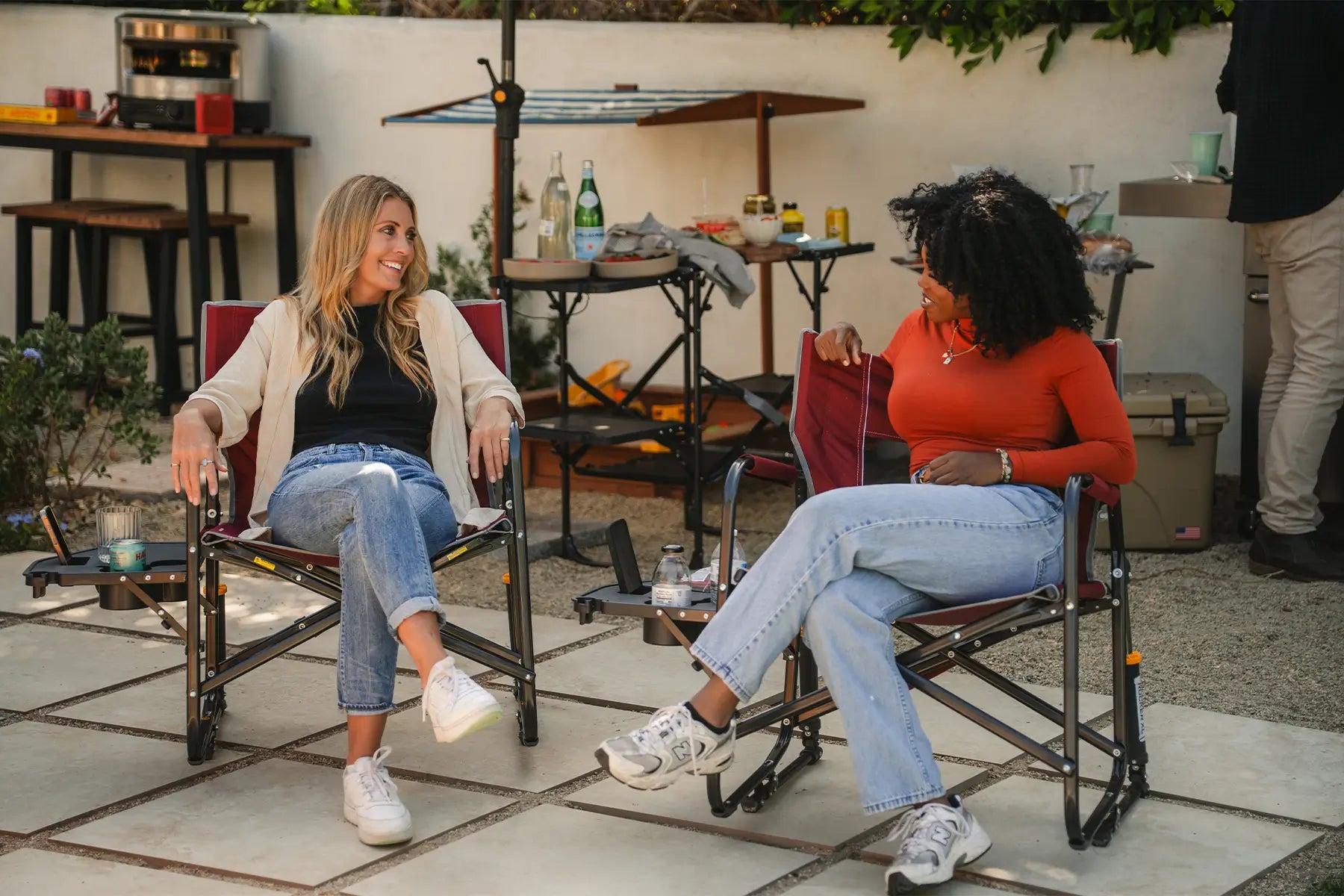 Two women conversing in their cinnamon freestyle rockers with side tables.