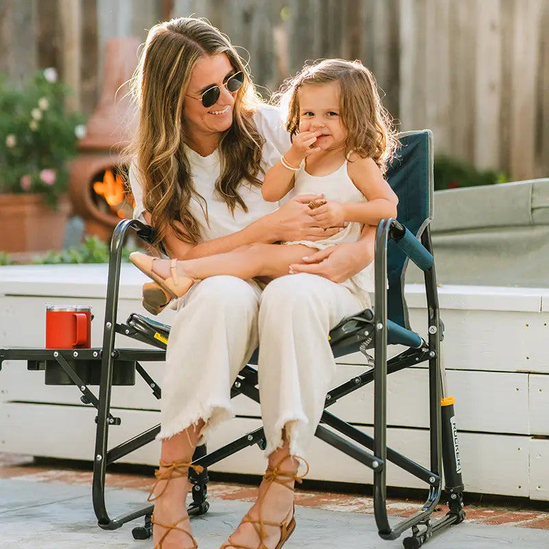 A woman holding a child next to a fire place while sitting in a Freestyle Rocker XL.