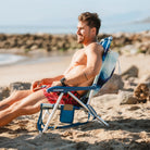 A man relaxing at the beach while sitting in a backpack beach chair.