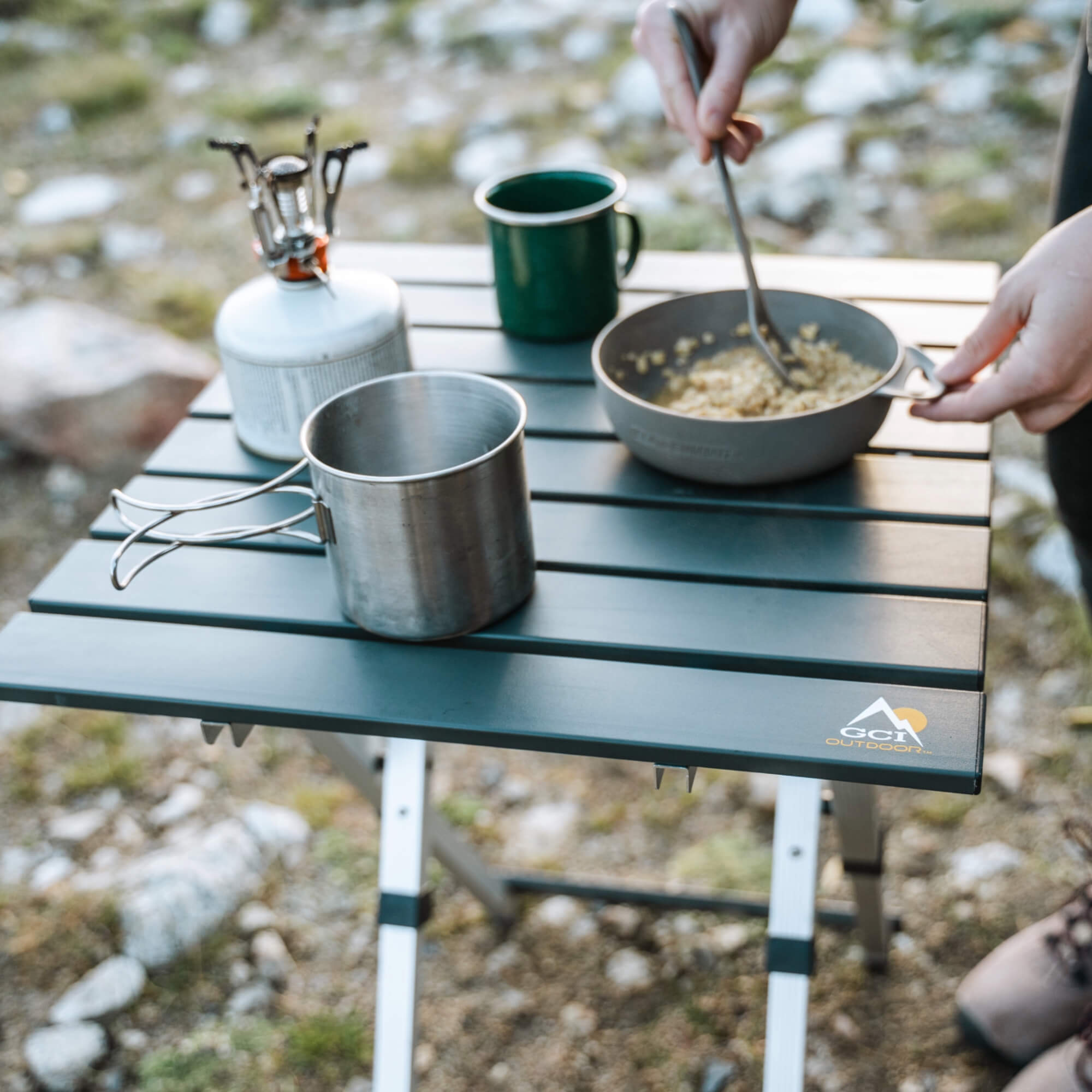 A person mixing food in a bowl thats resting on the compact camp table 20.