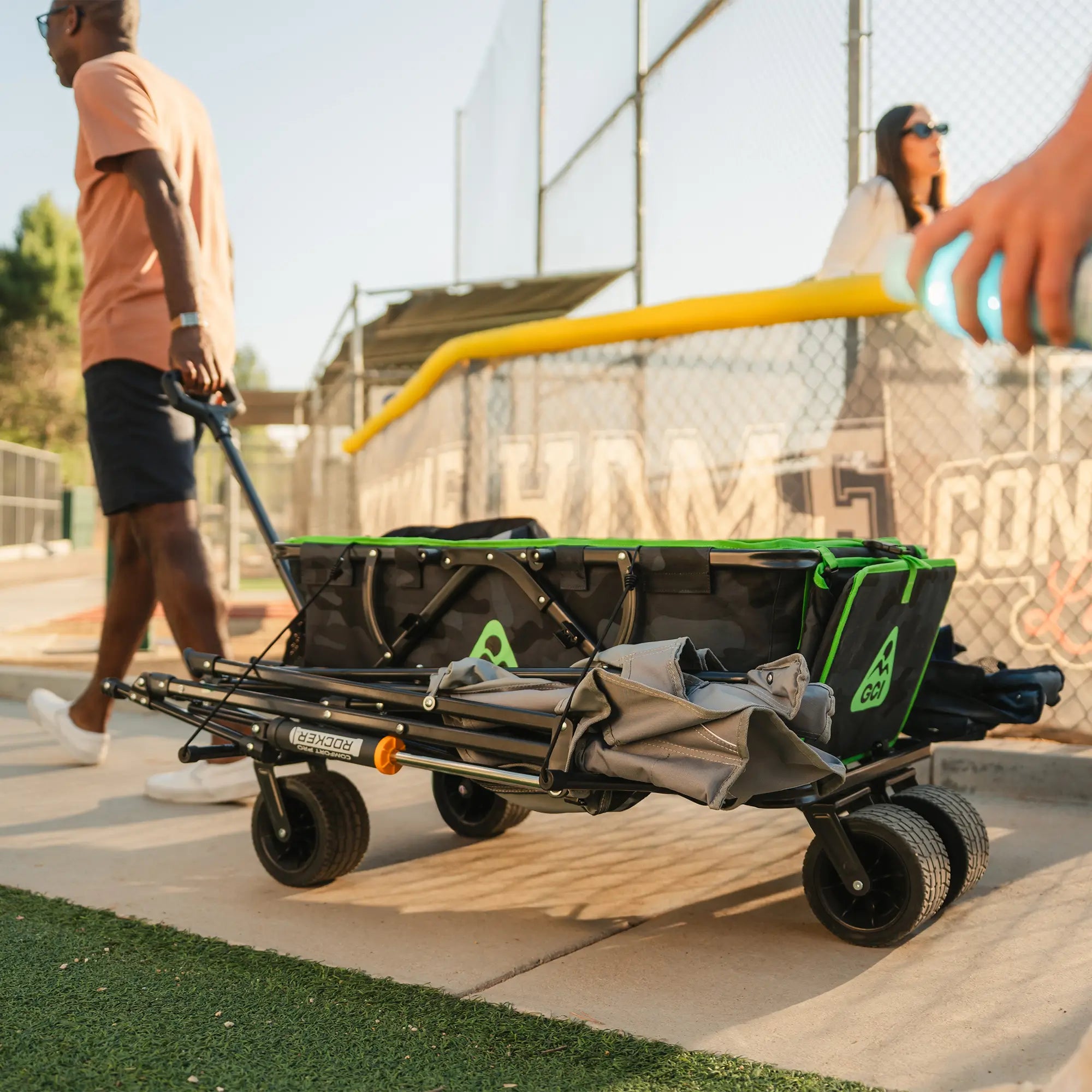 A man carrying a camo Go-Hauler near a baseball field that's loaded with Comfort Pro Rocker chairs.