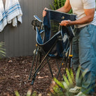 Person unfolding the heathered indigo Kickback Rocker in a backyard garden.