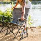 Woman setting down a heathered pewter Kickback Rocker beside a lakeside trail.