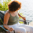 Woman placing a phone in the side pocket of the heathered pewter Kickback Rocker near a lake.