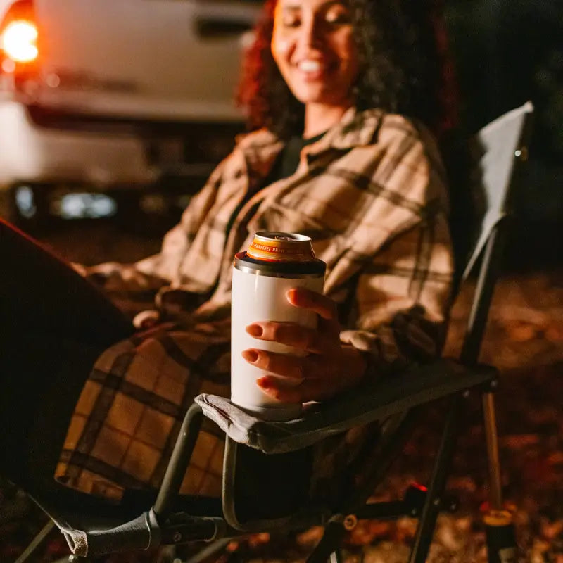 Woman holding a drink in the heathered pewter Kickback Rocker by a campfire at night.