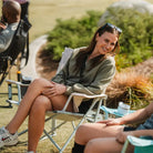 Woman smiles while relaxing in a Soft Neutral Leaf Kickback Rocker during an outdoor gathering.