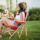 Woman enjoys a meal while seated in a Soft Pink Leaf Kickback Rocker on a sunny lawn.