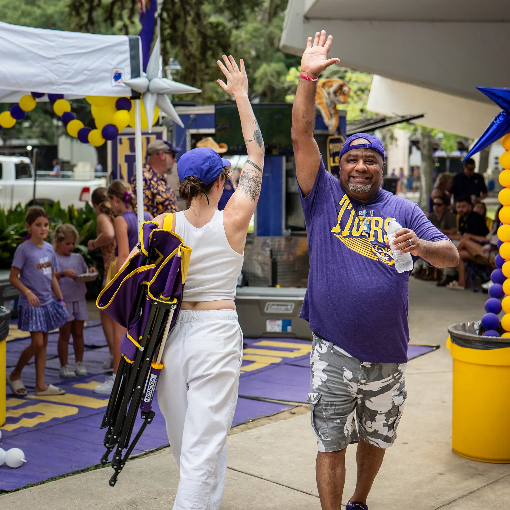 A man wearing an LSU tigers shirt high fiving a woman carrying an LSU comfort pro rocker on her shoulder.