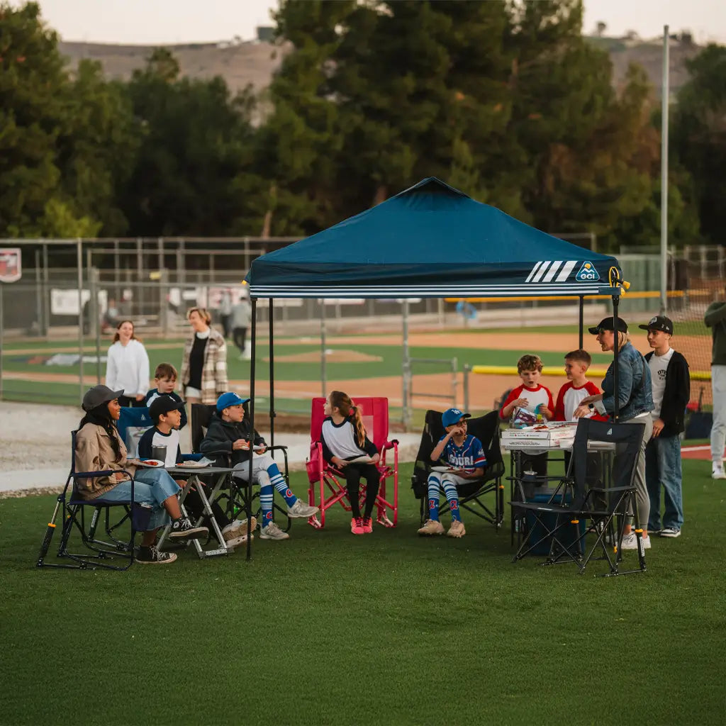 A family gathered sitting underneath the levrup canopy at a baseball field.