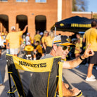 A man raising his hand to wave at somebody while sitting in an iowa state comfort pro rocker with "hawkeyes" text on the back of his chair.