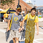 A parent and a student carrying their iowa state comfort pro rockers on their shoulder while walking through a tailgate party.