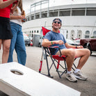A man watching a group of people play cornhole while sitting in an ohio state comfort pro rocker chair.