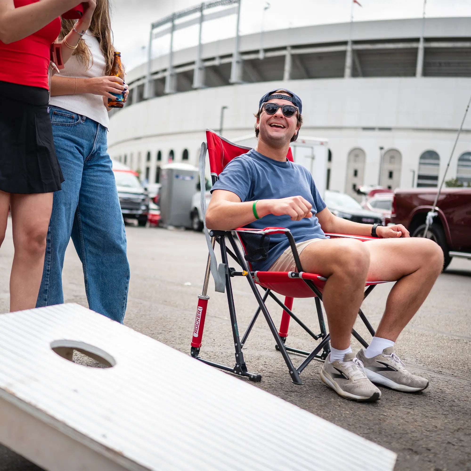 A man watching a group of people play cornhole while sitting in an ohio state comfort pro rocker chair.