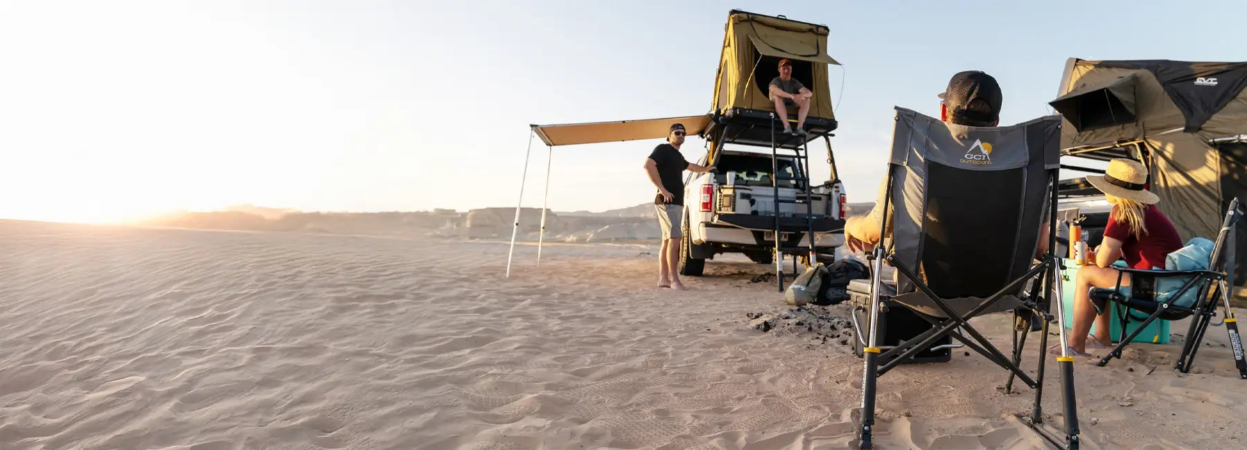 Group relaxing at a desert campsite with tents and trucks, using mercury gray Roadtrip Rockers in the sand.