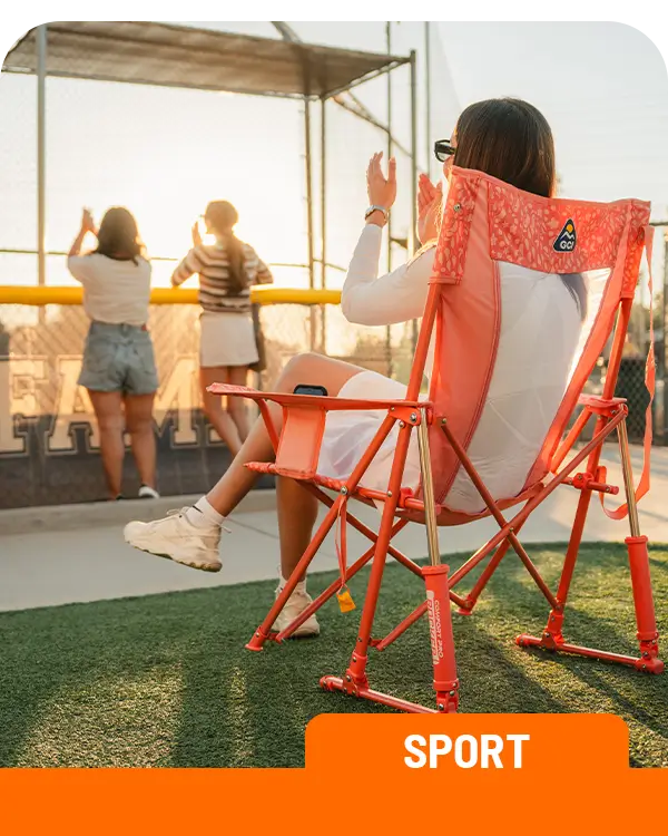 A woman cheering on a baseball game as she sits in a coral Comfort Pro Rocker.