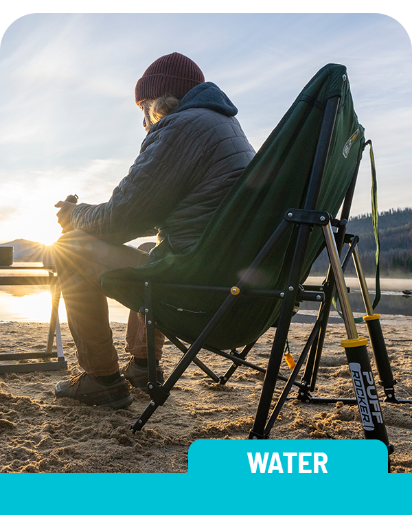 Person sitting on a green camping chair by a body of water at sunset. Labelled 'Water'