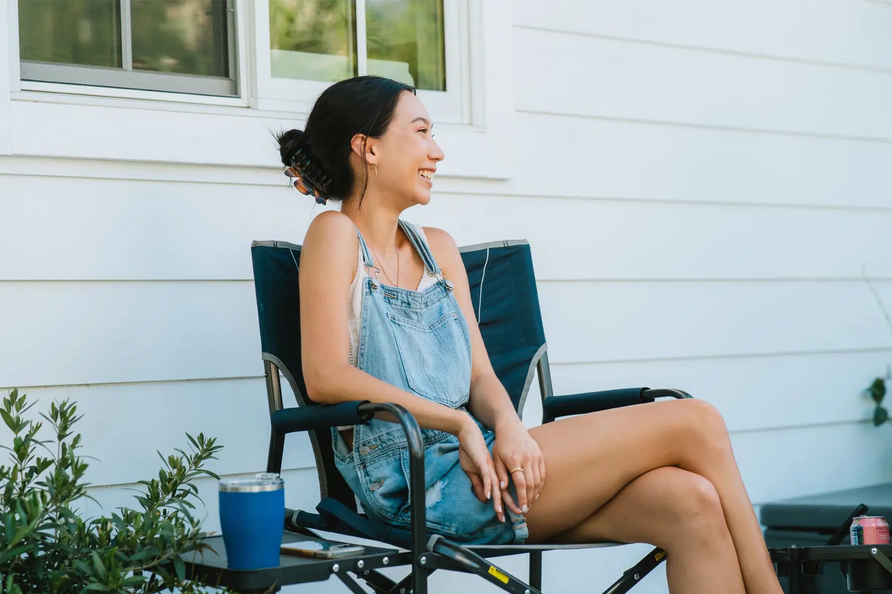 Woman sitting in a Slim-Fold Director’s Chair on a patio, smiling and holding a drink.