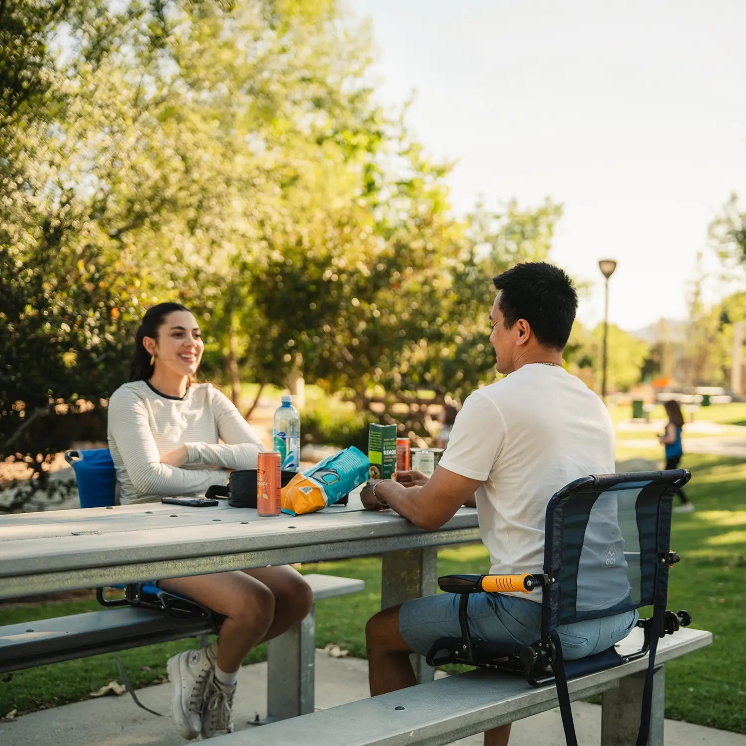 A couple having drinks together as they sit on a metal bench with their Big Comfort Stadium Chair and Stadium Rock-cliner.