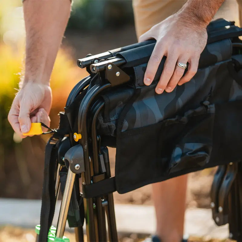 Close-up of hands unfolding the stealth camo Stowaway Rocker by pulling the yellow release strap.