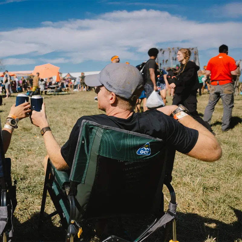 Man relaxing at an outdoor event in the hunter topo Stowaway Rocker, toasting with a drink.
